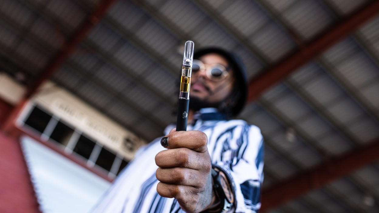 Black man blurred holding his hand out with a vape pen.
